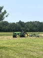 Jason in a John Deere tractor bailing hay in a field.